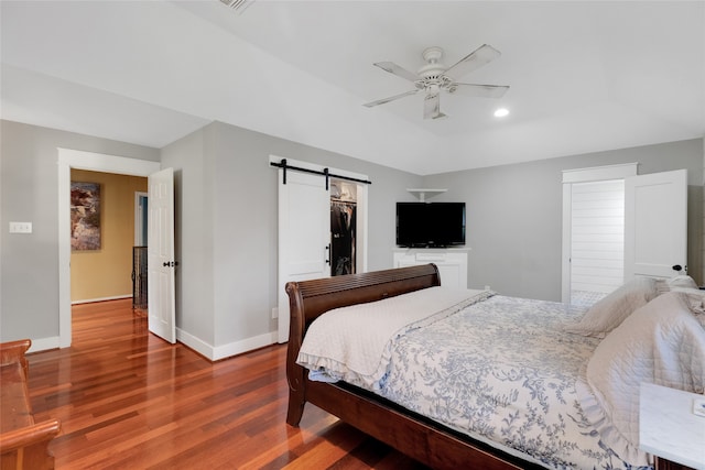 bedroom featuring a walk in closet, ceiling fan, a barn door, hardwood / wood-style floors, and a closet