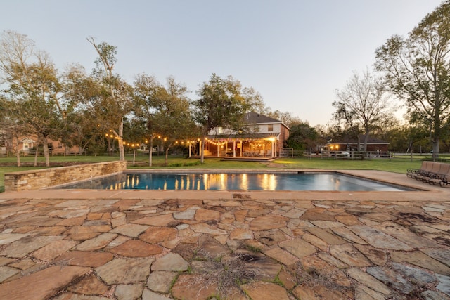 pool at dusk with a lawn and a patio area