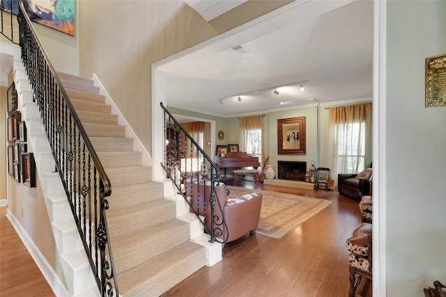 stairway with wood-type flooring, rail lighting, and ornamental molding