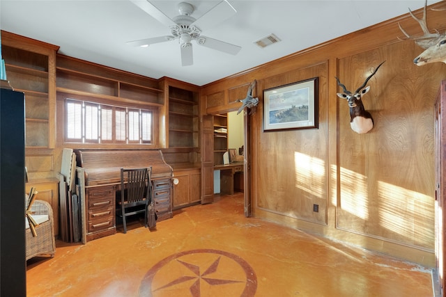 office area featuring wooden walls, ceiling fan, and built in desk