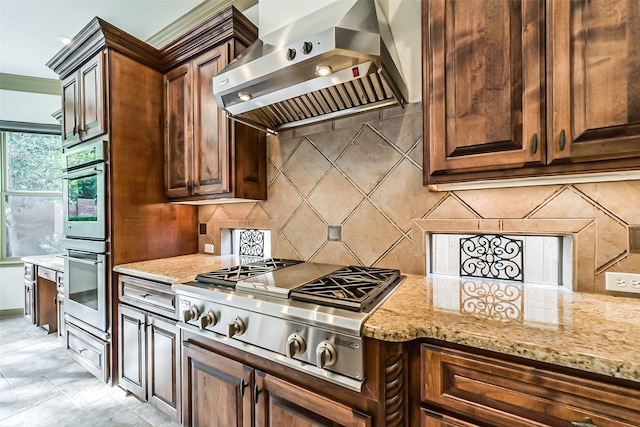 kitchen featuring tasteful backsplash, light stone counters, stainless steel appliances, and wall chimney range hood