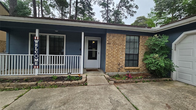 doorway to property with covered porch, brick siding, and an attached garage