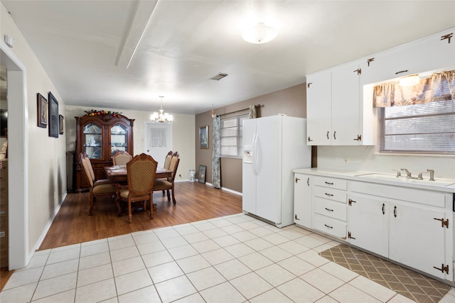 kitchen featuring white cabinetry, light hardwood / wood-style flooring, white refrigerator with ice dispenser, a chandelier, and pendant lighting