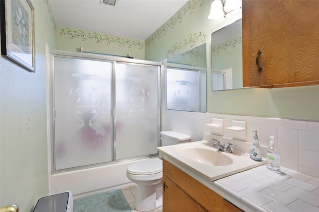 full bathroom with tile patterned flooring, combined bath / shower with glass door, toilet, decorative backsplash, and vanity