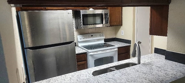 kitchen featuring light stone counters, sink, decorative backsplash, and stainless steel appliances