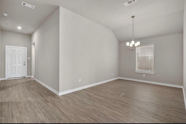 spare room featuring lofted ceiling, wood-type flooring, and an inviting chandelier