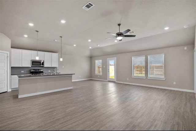 kitchen with white cabinets, hanging light fixtures, an island with sink, appliances with stainless steel finishes, and light hardwood / wood-style floors