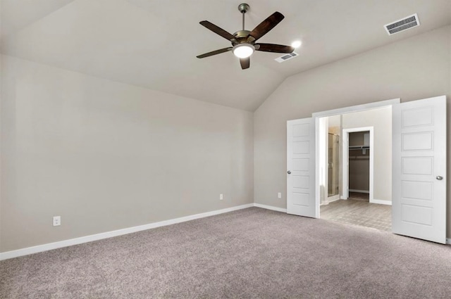 unfurnished bedroom featuring light colored carpet, vaulted ceiling, ceiling fan, a spacious closet, and a closet