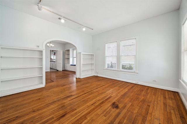 unfurnished living room featuring an inviting chandelier, track lighting, and hardwood / wood-style flooring