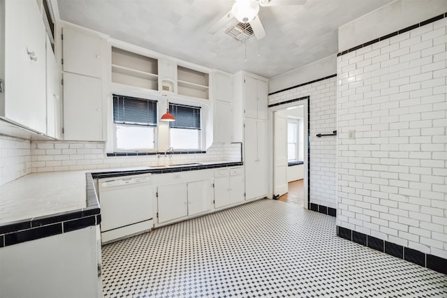 kitchen with ceiling fan, sink, white dishwasher, white cabinets, and tile walls