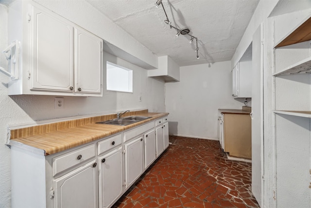 kitchen featuring a textured ceiling, white cabinetry, sink, and track lighting