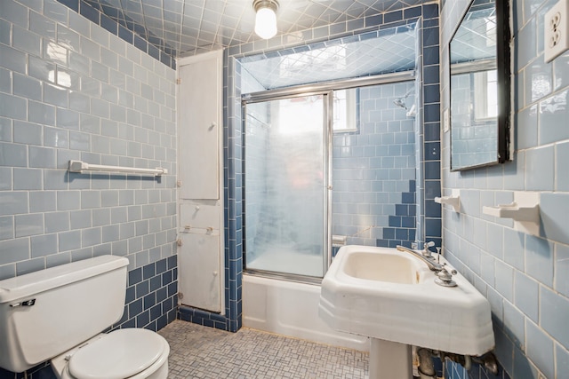 full bathroom with combined bath / shower with glass door, sink, tile walls, tile patterned flooring, and toilet