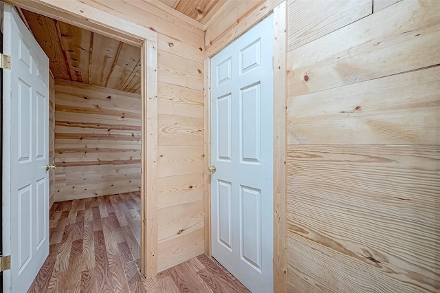 hall featuring light wood-type flooring, wooden walls, and wooden ceiling