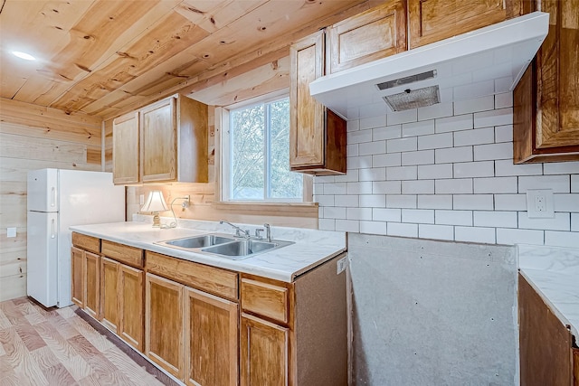 kitchen featuring white refrigerator, extractor fan, wood walls, and sink