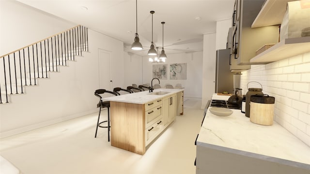 kitchen featuring stainless steel fridge, a breakfast bar, a kitchen island with sink, sink, and hanging light fixtures