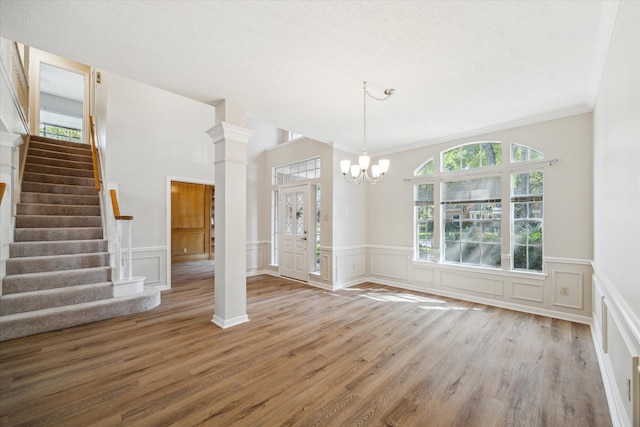 interior space featuring decorative columns, a textured ceiling, crown molding, an inviting chandelier, and hardwood / wood-style floors