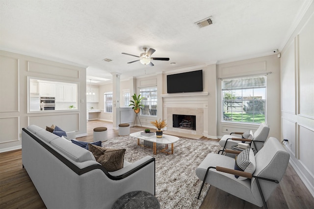 living room with ceiling fan, dark hardwood / wood-style flooring, crown molding, and a tiled fireplace