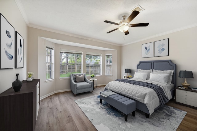 bedroom with a textured ceiling, light hardwood / wood-style flooring, ceiling fan, and ornamental molding