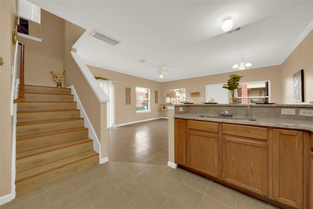 kitchen featuring light stone countertops, sink, crown molding, light tile patterned floors, and ceiling fan with notable chandelier