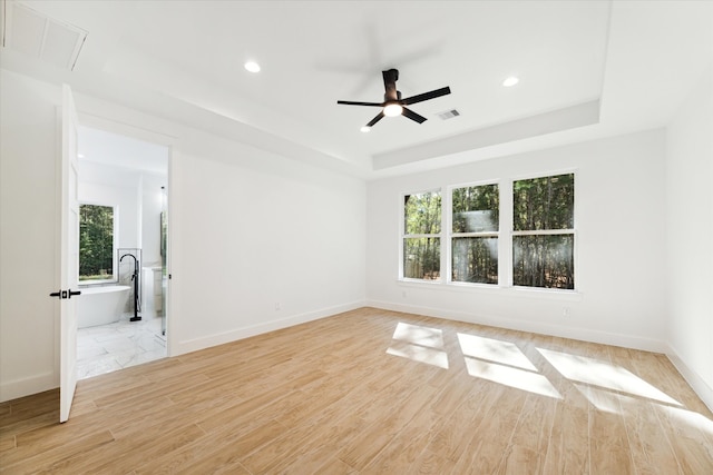 unfurnished room featuring a tray ceiling, ceiling fan, and light hardwood / wood-style floors