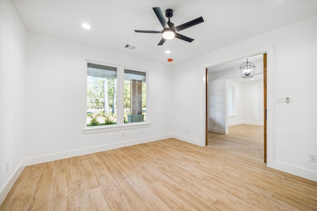 spare room featuring ceiling fan with notable chandelier and light wood-type flooring