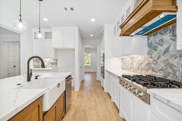 kitchen with light stone countertops, stainless steel appliances, white cabinets, custom range hood, and light wood-type flooring