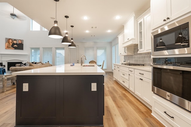 kitchen featuring white cabinets, sink, hanging light fixtures, an island with sink, and light hardwood / wood-style floors