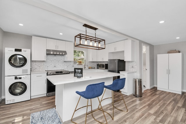 kitchen featuring stainless steel appliances, pendant lighting, light hardwood / wood-style floors, white cabinets, and stacked washer and clothes dryer