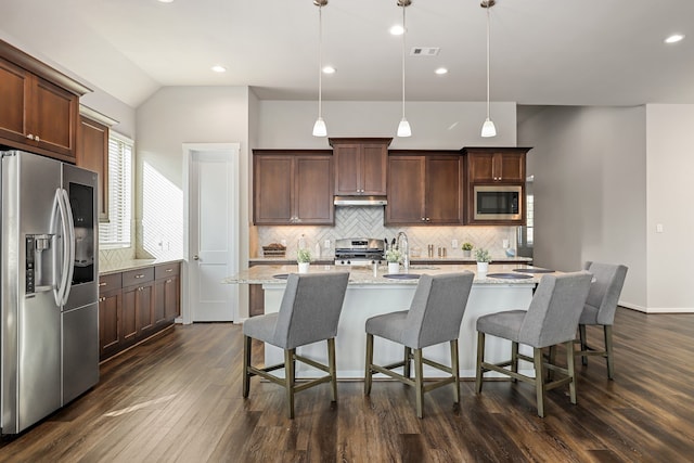 kitchen featuring dark hardwood / wood-style flooring, stainless steel appliances, a kitchen island with sink, decorative light fixtures, and lofted ceiling