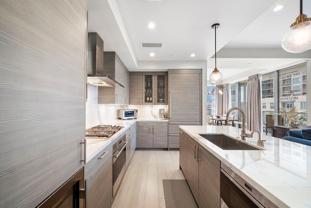 kitchen with pendant lighting, sink, light hardwood / wood-style flooring, wall chimney exhaust hood, and stainless steel appliances