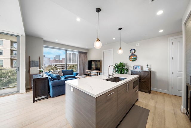 kitchen with sink, light hardwood / wood-style flooring, pendant lighting, a center island with sink, and dark brown cabinets