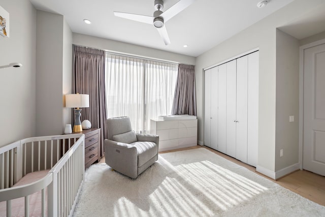 bedroom featuring ceiling fan, light wood-type flooring, a crib, and a closet