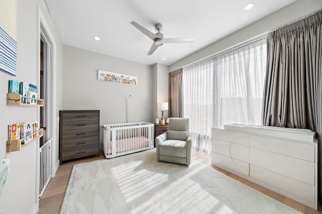 bedroom with light wood-type flooring, a nursery area, and ceiling fan