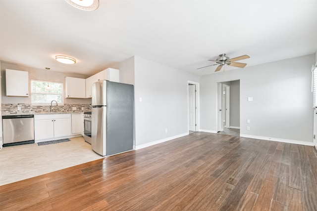 kitchen featuring appliances with stainless steel finishes, light wood-type flooring, backsplash, sink, and white cabinetry