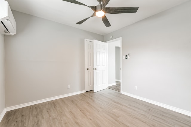 unfurnished bedroom with an AC wall unit, ceiling fan, and light wood-type flooring