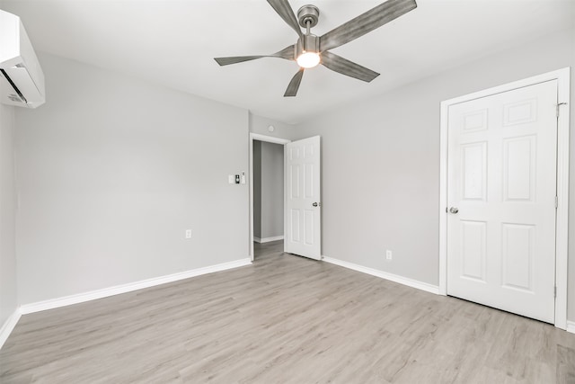 unfurnished bedroom with a wall mounted AC, light wood-type flooring, and ceiling fan