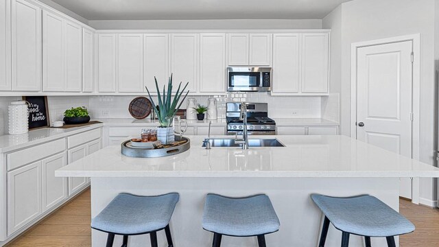 kitchen featuring white cabinets, appliances with stainless steel finishes, a center island with sink, and light hardwood / wood-style flooring