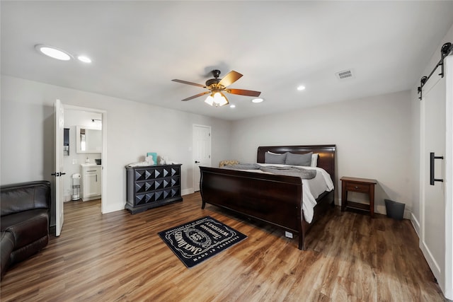 bedroom with hardwood / wood-style floors, ceiling fan, a barn door, and ensuite bath