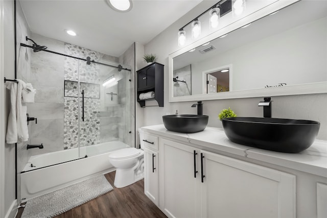 full bathroom with toilet, hardwood / wood-style floors, vanity, and combined bath / shower with glass door