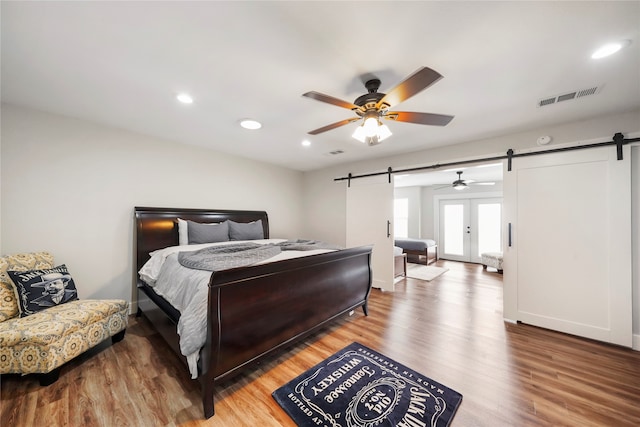 bedroom with french doors, wood-type flooring, a barn door, and ceiling fan