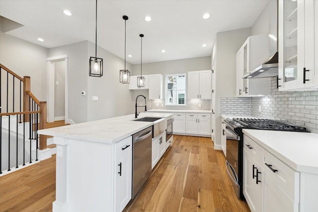 kitchen featuring white cabinetry, a center island with sink, stainless steel appliances, and light hardwood / wood-style floors