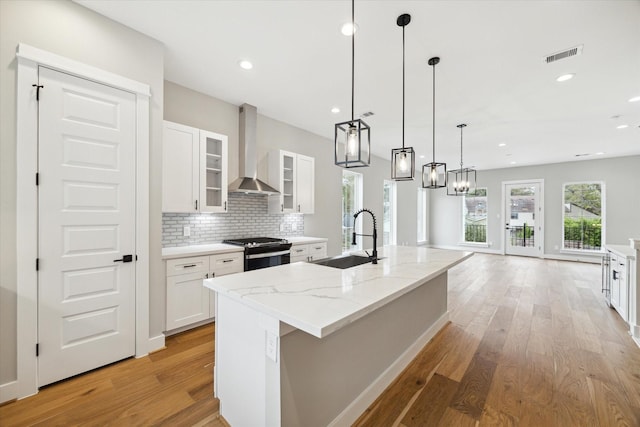 kitchen featuring a center island with sink, wall chimney exhaust hood, sink, and stainless steel range