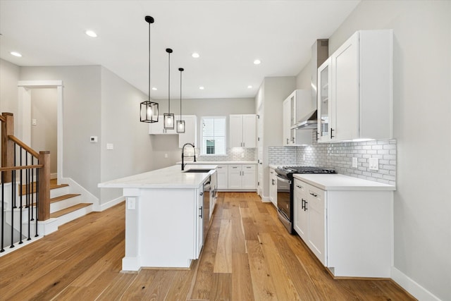 kitchen with white cabinets, a center island with sink, sink, light wood-type flooring, and appliances with stainless steel finishes