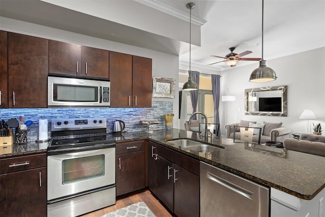 kitchen with appliances with stainless steel finishes, dark stone counters, sink, decorative light fixtures, and light hardwood / wood-style floors