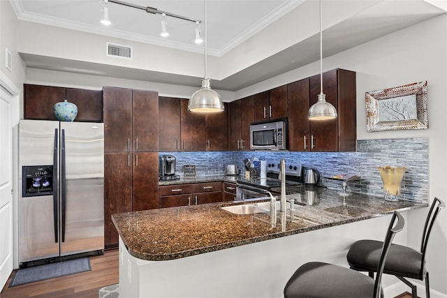 kitchen with dark stone countertops, pendant lighting, stainless steel appliances, and wood-type flooring