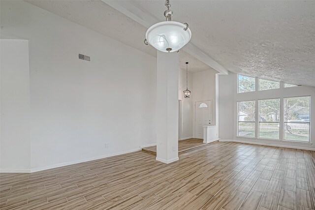 unfurnished living room featuring a textured ceiling, vaulted ceiling with beams, and light hardwood / wood-style flooring