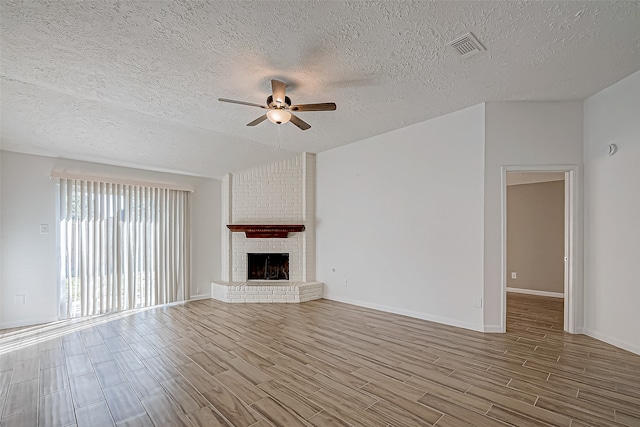 unfurnished living room featuring ceiling fan, a fireplace, a textured ceiling, and light wood-type flooring