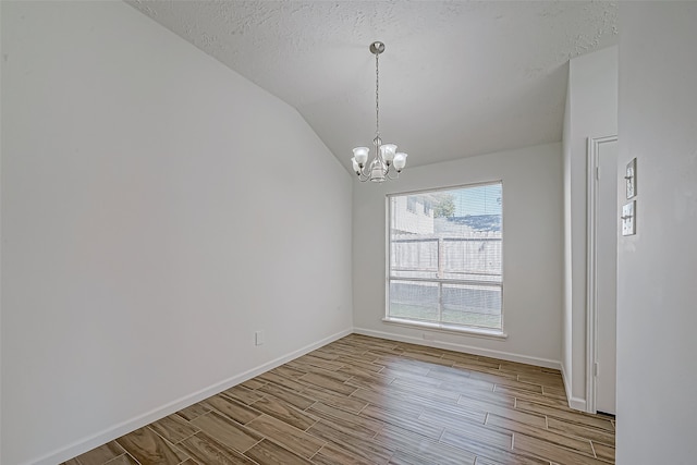 spare room with a chandelier, a textured ceiling, light hardwood / wood-style floors, and vaulted ceiling