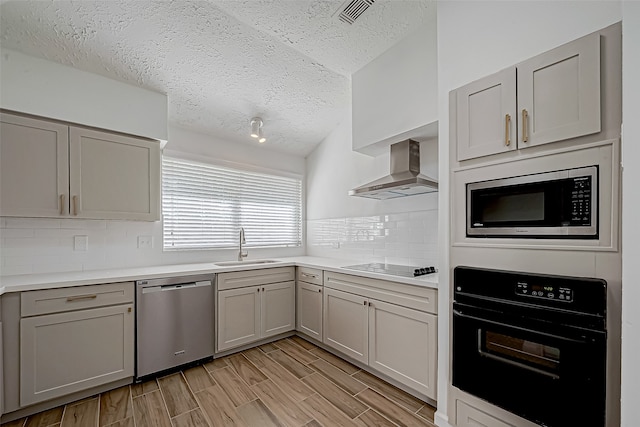 kitchen with wall chimney range hood, light hardwood / wood-style floors, gray cabinetry, and black appliances