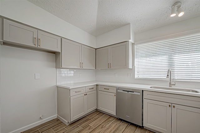 kitchen with sink, stainless steel dishwasher, a textured ceiling, decorative backsplash, and light wood-type flooring